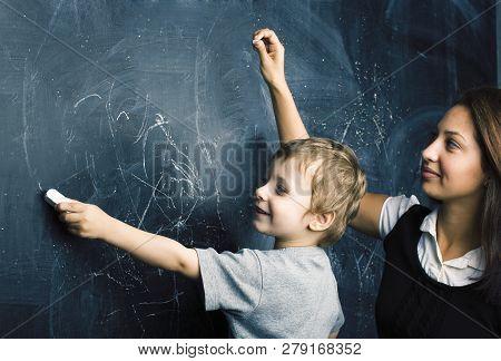 Little Cute Boy In Glasses With Young Real Teacher, Classroom Studying At Blackboard School Kido
