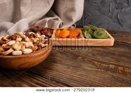 Dates, Dried Apricots And Kiwis In A Compartmental Dish And Assortment Of Nuts In Wooden Bowl On A D