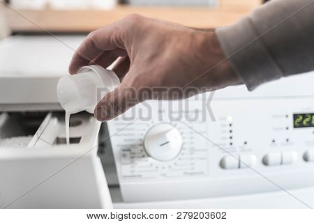 Close-up Of Person Using Dosing Aid To Fill Fabric Softener Into Washing Machine