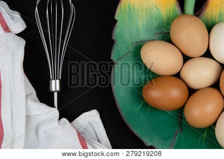 Top View Of Hen Eggs In A Leaf Shaped Plate And An Eggbeater On A Black Background.