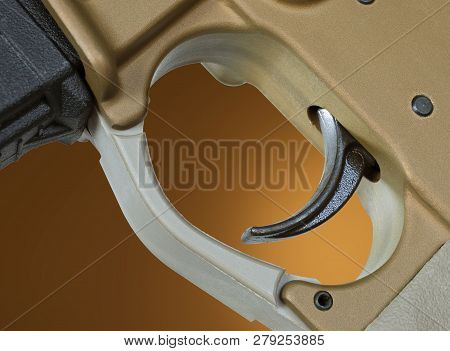 Trigger On An Ar-15 That Is Gold In Color On A Brown Background