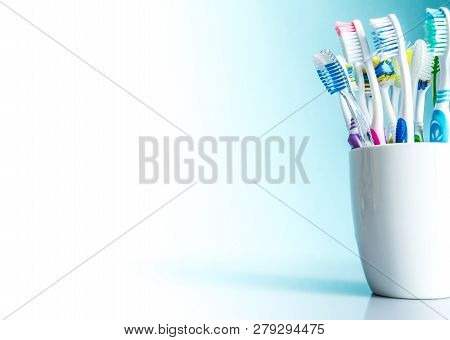 Multi-colored Toothbrushes In A White Mug Close-up With A Gradient Background From White To Blue Wit