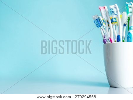 Multi-colored Toothbrushes In A White Mug Close-up In The Bathroom On A Mirror Table On A Blue Backg
