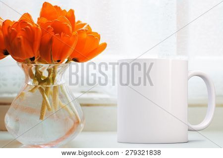 Blank Mug Next To A Bunch Of Orange Tulips In A Glass Vase On A Window Ledge. Perfect For Businesses