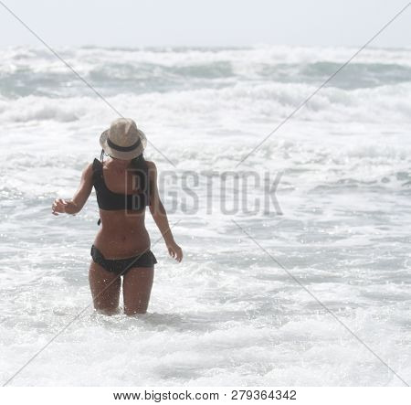 Beautiful Girl With Hat At The Sea Who Walking In The Water. The Sea In The Background. Sabaudia, La