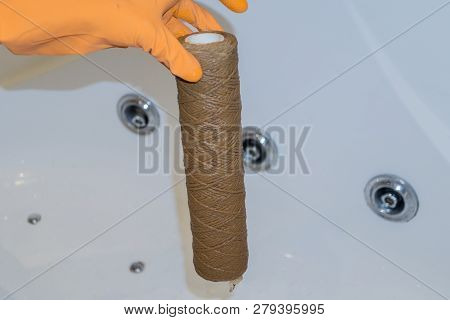 Hand Holding Dirty Water Filter Cartridge Over The Bathhub