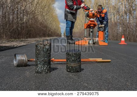 Worker Cut By The Core Sampler Samples Of Asphalt Concrete On The Road. Asphalt Concrete Cores Close