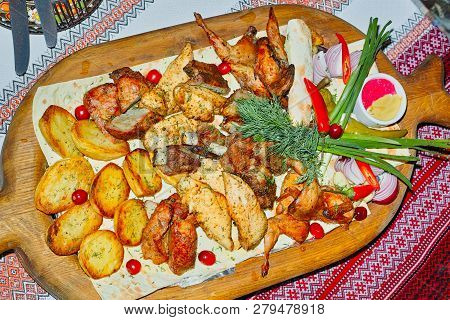Wooden Board With Grilled Meat And Baked Potatoes With Dill On Pita Bread. Served With Pepper, Herbs