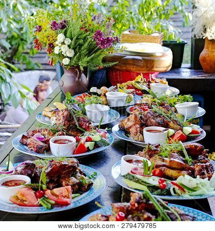 Set The Table With Grilled Meat With Vegetables And Greens. Decorated With Flowers.