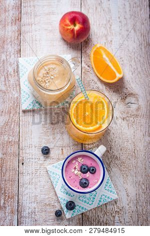 A Mix Of Three Smoothies With Blueberry, Orange And Peach On A Wooden Background, Top View