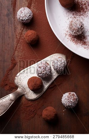 Chocolate Sweets With Cocoa And Coconut Chips On A White Plate, Top View, Selective Focus