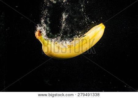 Sprkling Yellow Banana Falls In Water On Black Background