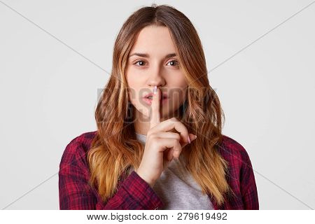 Beautiful Tender Woman Males Silence Gsture, Looks Secretly At Camera, Dressed In Casual Outfit, Has
