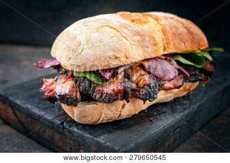Traditional barbecue pulled pork piece of Bosten butt as sandwich with lettuce as closeup on a black board