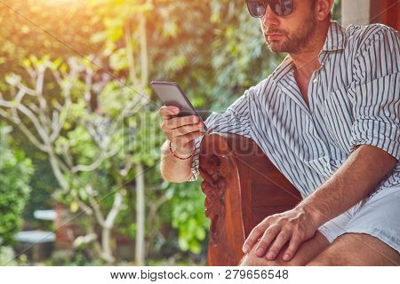 Man Using Smart Phone On A Terrace Sofa In Summertime.
