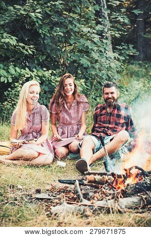 Happy Friends At Campfire. Bearded Man And Women Smile At Bonfire. Hipster In Palid Shirt And Girls 