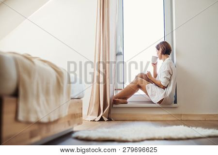 A Young Woman With Night Shirt Sitting By The Window In The Morning.