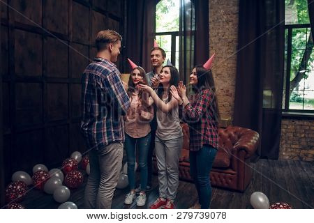Friends In Party Hats Celebrate Birthday At A Party With Cupcake In A Loft. Smiling Frinds Sing Birt