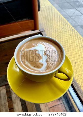 Flat White Coffee With Foamy Milk In Yellow Cup Served At Cafe Shop