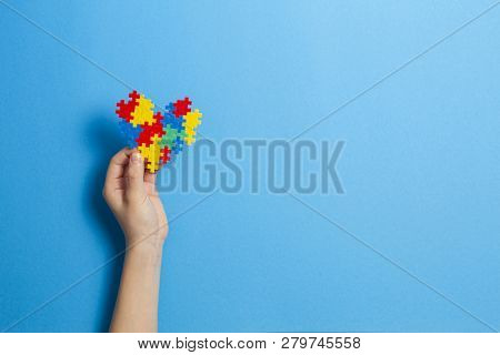 Child Hand Holding Colorful Heart On Blue Background. World Autism Awareness Day Concept