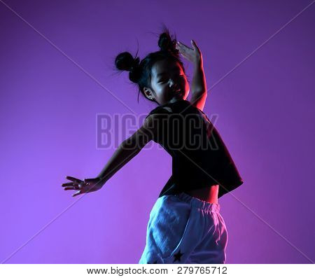 Joyfull Asian Kid Girl In Shirt And Pants With Stars On Purple Background Dances And Jumps