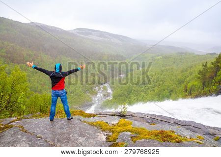 Young Man Looking On View Of Green Mountain From Valnesforsen Waterfall In Norway