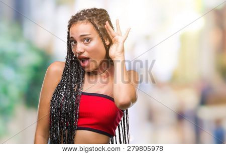 Young braided hair african american with pigmentation blemish birth mark over isolated background smiling with hand over ear listening an hearing to rumor or gossip. Deafness concept.