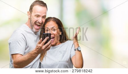 Middle age hispanic couple texting message on smartphone ver isolated background very happy and excited, winner expression celebrating victory screaming with big smile and raised hands