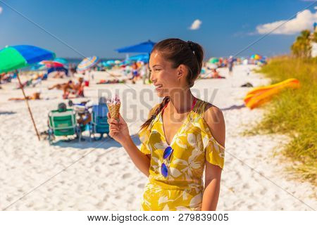 Ice cream Asian woman eating cone on Flordia beach walking in summer sun laughing happy with cherry frozen sorbet dessert. Young people lifestyle.