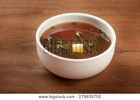 A Photo Of A Bowl Of Miso Shiru Soup With Tofu, Scallions, And Wakame Seaweed, On A Dark Rustic Wood