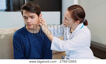 Woman Doctor Puts A Hearing Aid On A Young Guy.