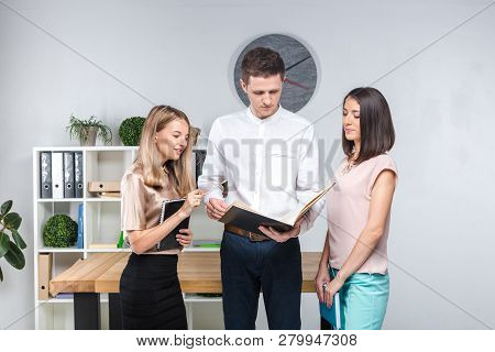 Theme Business, Teamwork And Partnerships. A Group Of Young People, Three People, Stand In An Office