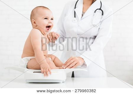Weight Measuring. Adorable Little Baby Sitting On Scales , Medical Check Up With Female Pediatrician