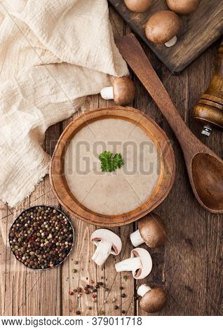 Wooden Plate Of Creamy Chestnut Champignon Mushroom Soup With Wooden Spoon, Pepper And Kitchen Cloth