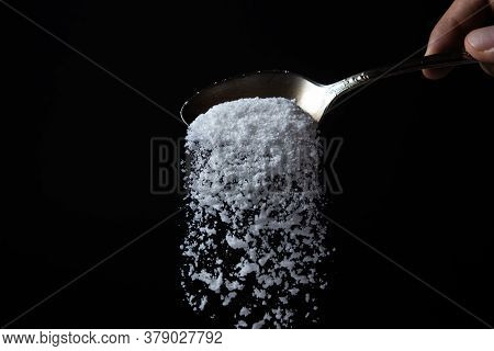 Salt Is Poured From A Spoon On A Black Background. Excessive Salt Intake. Coarse Salt