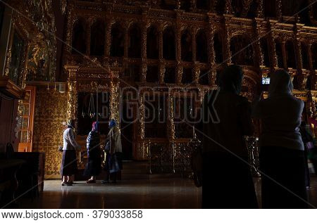 Sergiyev Posad, Russia - June 26, 2019: Female parishioners at golden decorated interior of Trinity Lavra of St. Sergius monastery. Dark room with natural poor light