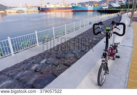 Geoje, South Korea - June 15, 2017: Brompton Folding Bike Parks On The Street Across Dsme Shipbuilde
