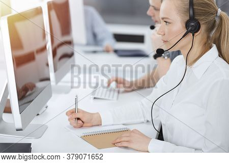 Call Center. Group Of Casual Dressed Operators At Work. Blond Business Woman In Headset At Customer 
