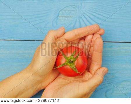 Womans Hands With Red Tomato On A Blue Background. Close-up. Proper Nutrition.