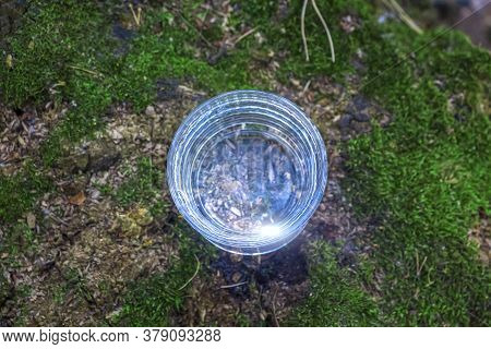Glass Of Clean Fresh Water On Tree Stump With Moss Against Green Natural Background. Spring Ecologic