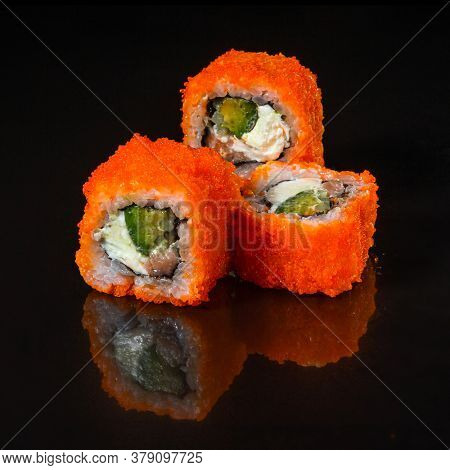California roll sushi with salmon, cucumber, avocado, cream cheese, red masago caviar over black background. Sushi menu, Japanese food. 