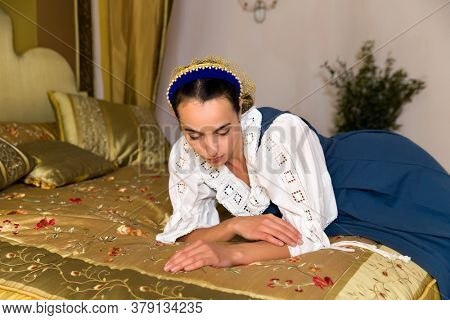 Dutch Master style portrait of a beautiful young woman in authentic renaissance costume lying on a luxury antique canopy bed in a golden bedroom of a medieval French castle with property release