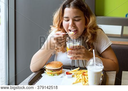 Asian Young Girl Sitting Table Indoors And Eating Ice Cream With Pleasure. Fart Her Hamburger, Fries