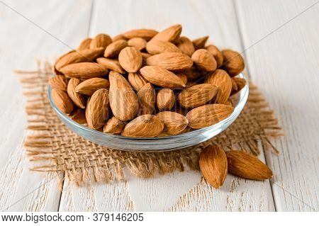 Tasty Raw Almonds In A Glass Saucer On A White Wood Table. Unroasted Nuts As Antioxidant And Protein