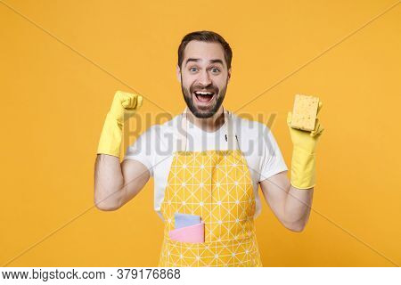 Excited Young Man Househusband In Apron Rubber Gloves Hold Cleaning Sponge Rag While Doing Housework