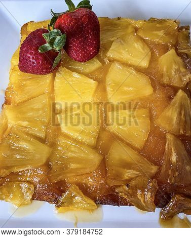 Upside-down Pineapple Cake Decorated With Red Whole Strawberries On A Serving Plate