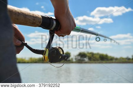 Fishing Rod Wheel Close Up In Young Man Hands On The Beautiful View Of Water And Clouds