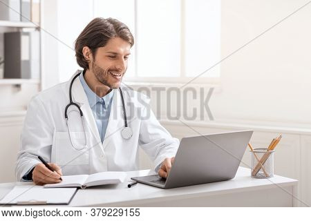 Online Concilium. Young Doctor Conversating With Colleagues Via Laptop Online, Empty Space