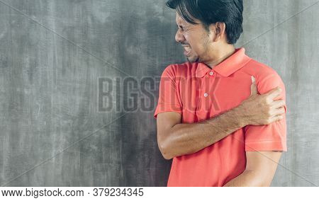 Young Asian Man Suffering From Shoulder Pain On Cement Wall Background With Copy Space, Problems And