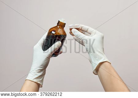 Close Up Of Hands In Gloves Showing Cough Syrup On Light Pink Background. The Concept Of Preventive 
